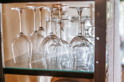 Many wineglasses placed upside down on glass shelf in cupboard in light modern restaurant