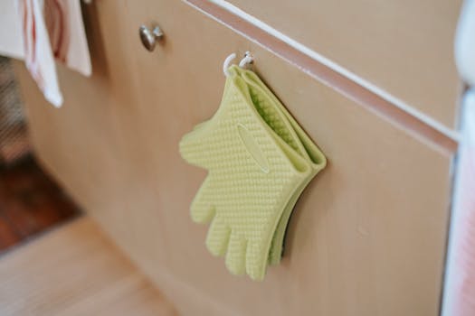 Green silicone oven gloves hang on a kitchen cabinet, showcasing modern design and functionality.