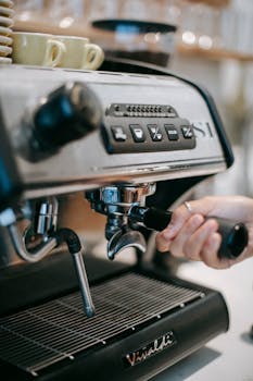 Crop anonymous bartender putting portafilter into modern coffee maker with cups on top at work