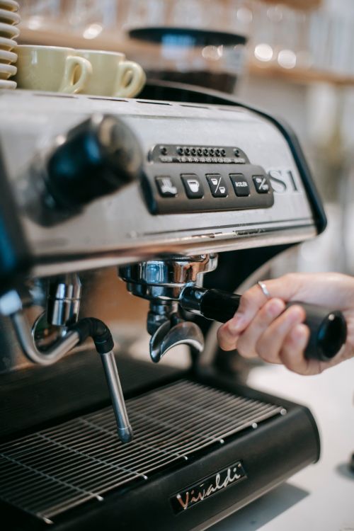 Free Crop anonymous bartender putting portafilter into modern coffee maker with cups on top at work Stock Photo