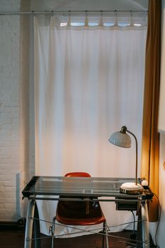 Rectangular shaped table with lamp near chair and curtain in empty room in house