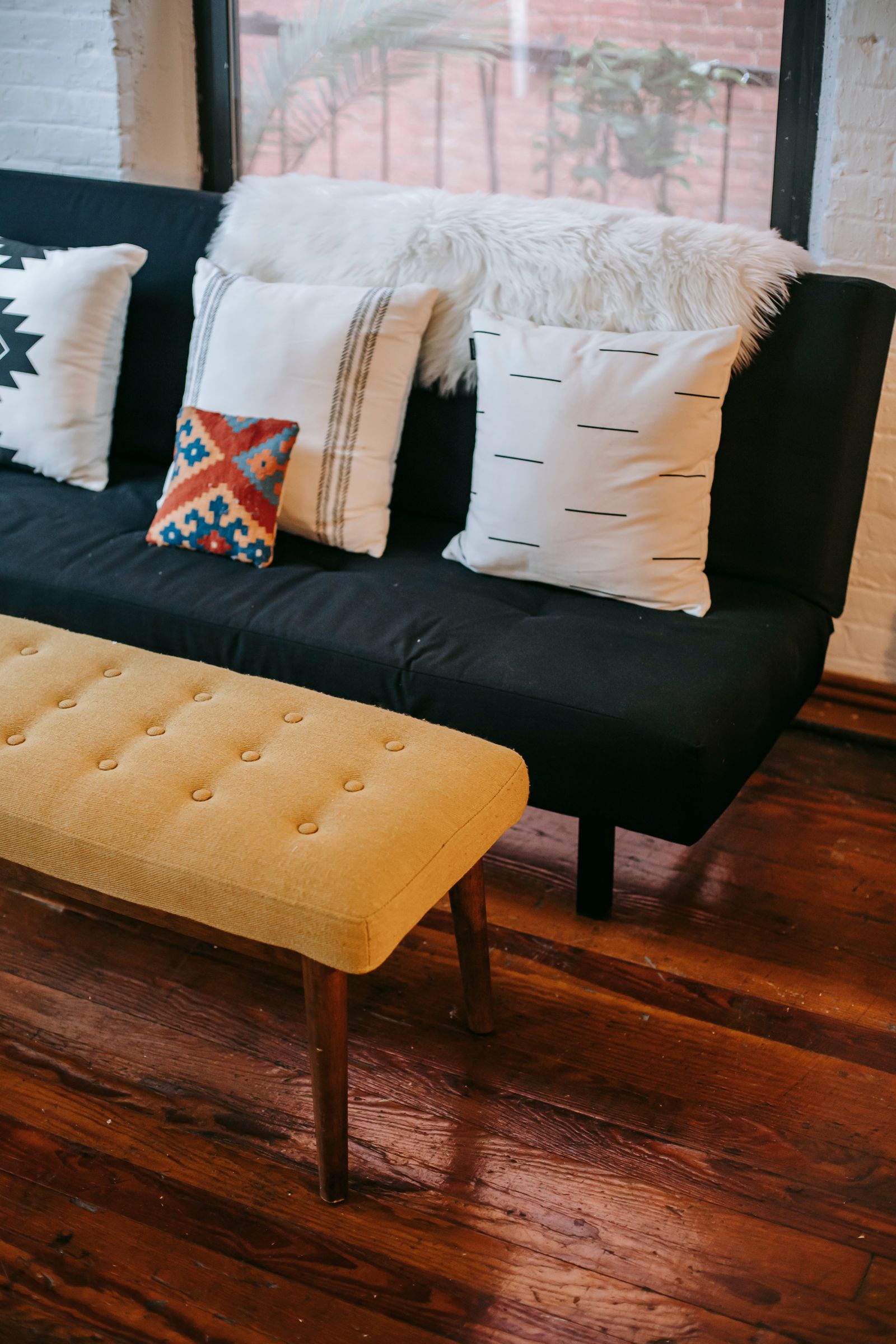Sofá com almofadas decorativas ao lado de um apoio estofado amarelo.