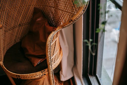 From above of wicker armchair with pillow placed near window in cozy apartment