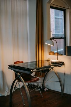 Interior of contemporary room with glowing lamp on table placed near curtain and aperture at low light in modern apartment