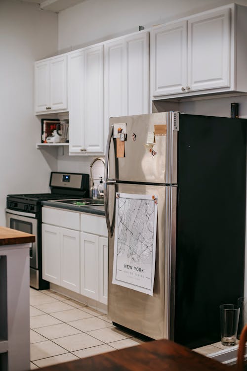 Free Modern light kitchen furnished with refrigerator and white cupboards placed near stove oven in modern cozy apartment with tiled floor Stock Photo