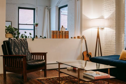 Free Modern room with sofa and guitar placed near glass table and soft armchair in living room with potted plant and windows Stock Photo