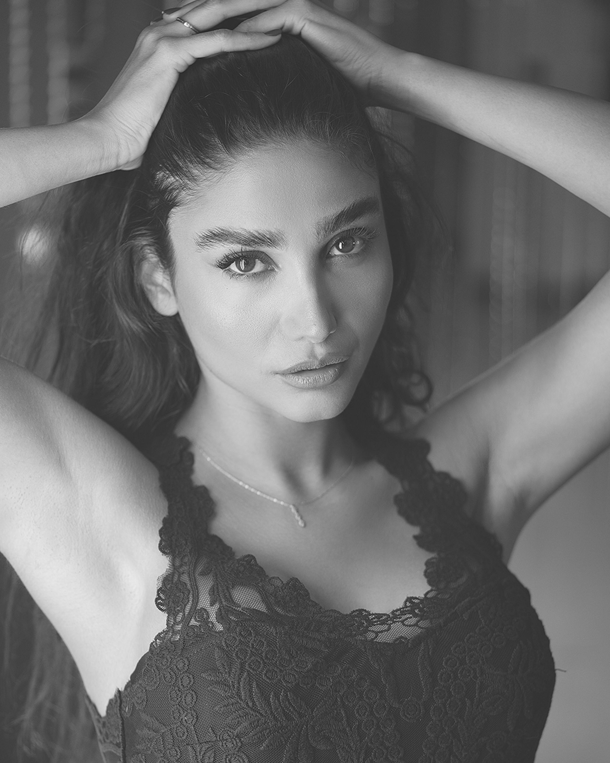 Elegant black and white portrait of a woman posing with hands on her head, highlighting beauty and emotion.