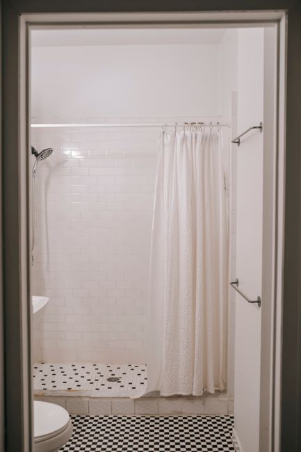 Shower cabin with curtain on beam against tiled wall and toilet bowl in bathroom at home