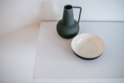 From above of empty vase with handle near round shaped bowl on white desk at home