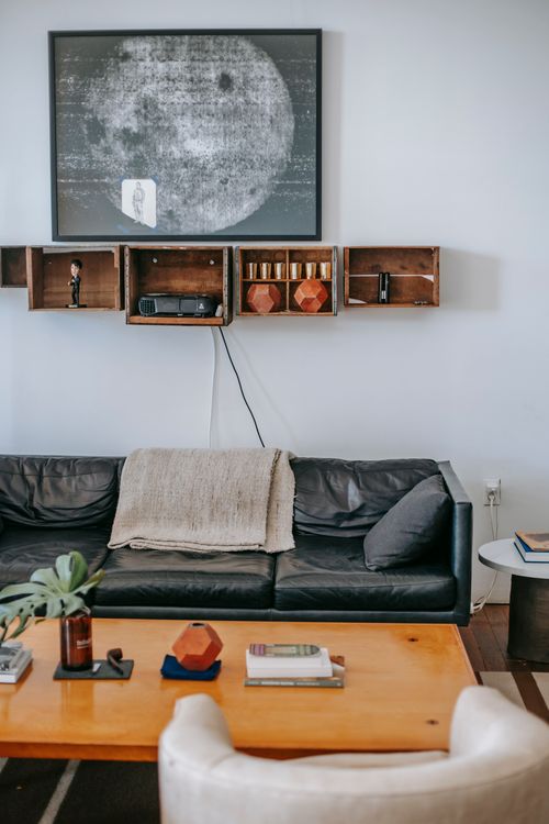 Free Comfortable black leather couch located under wooden bookshelves and contemporary painting on white wall and near table with white armchair in living room Stock Photo