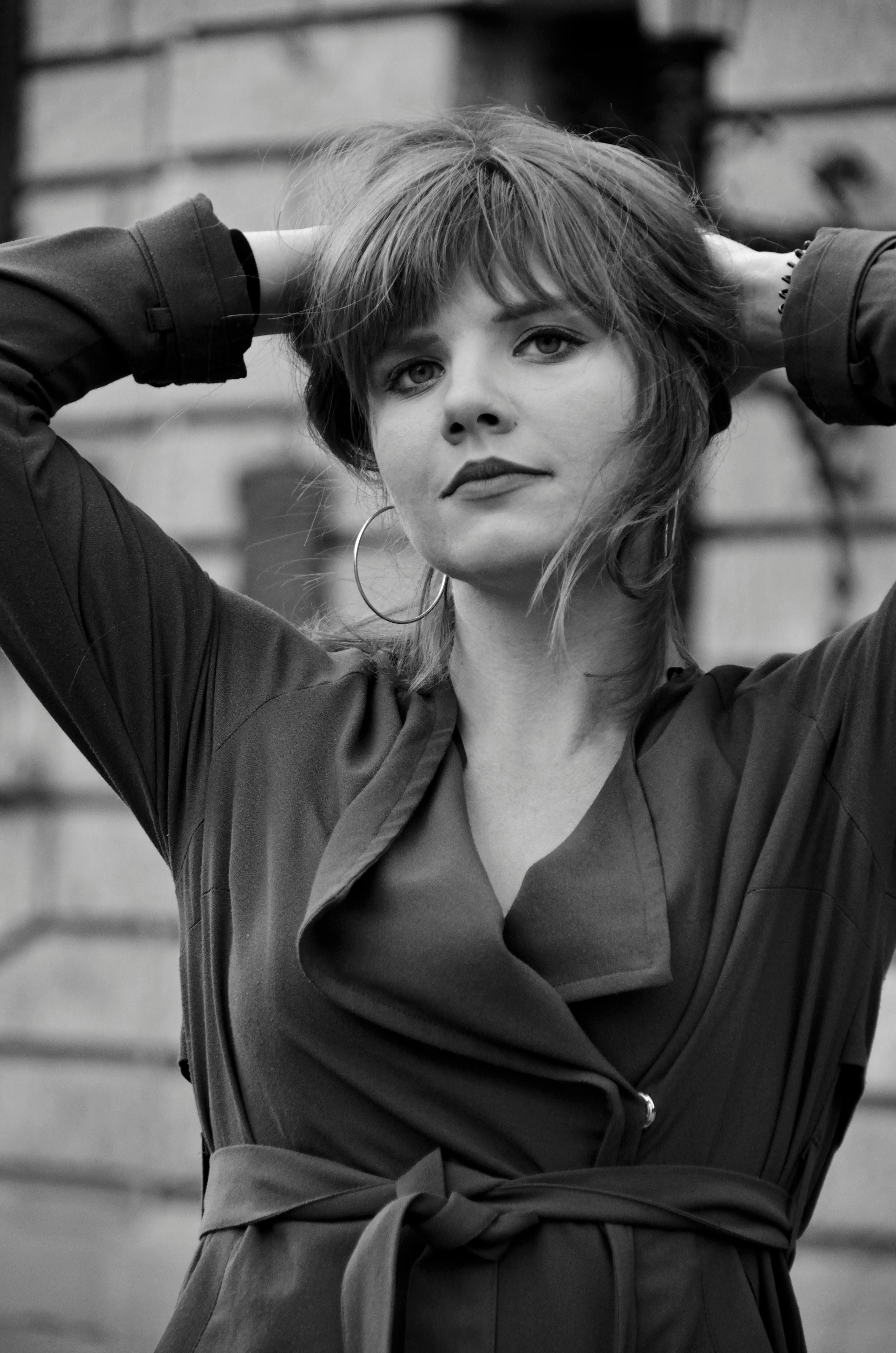 A grayscale portrait of a young woman with hands on head, exuding confidence and elegance.