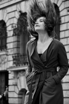 Grayscale portrait of a woman with flowing hair in front of classic architecture.