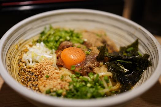 Appetizing bowl of ramen with egg yolk, beef, seaweed, and scallions, perfectly presented.