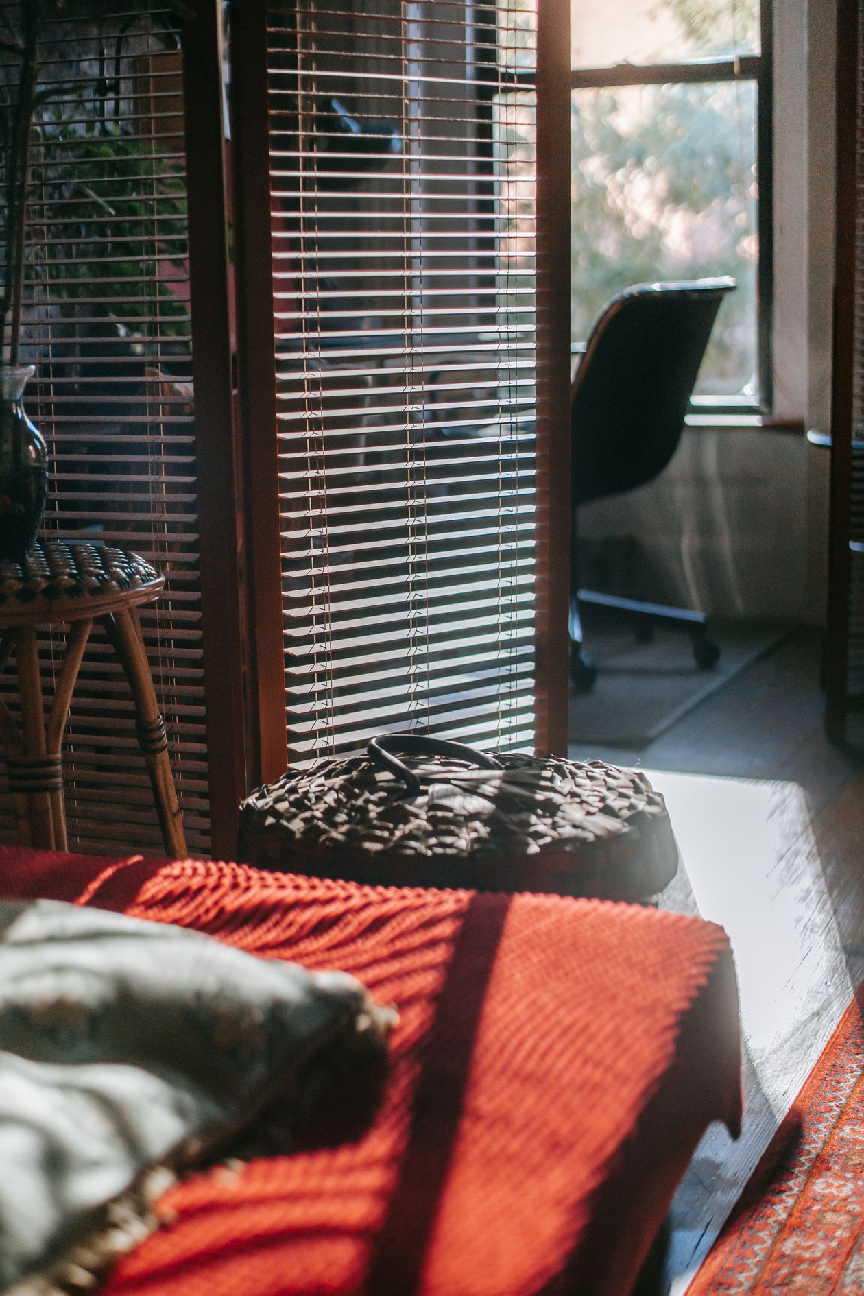 A warm cream-toned studio with a tall bookshelf between a sofa nook and bedroom, lit by a floor lamp and candles