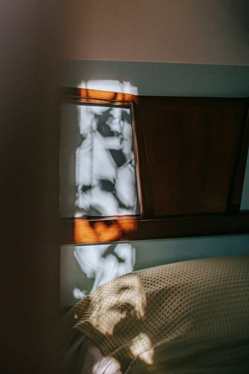 Free Big wooden bed with soft pillow covered with knitted plaid located in apartment near blue wall in shadow of morning sun rays Stock Photo