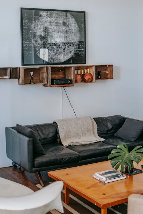 Comfortable black leather couch with cushions  near wooden coffee table and white armchair in modern cozy living room