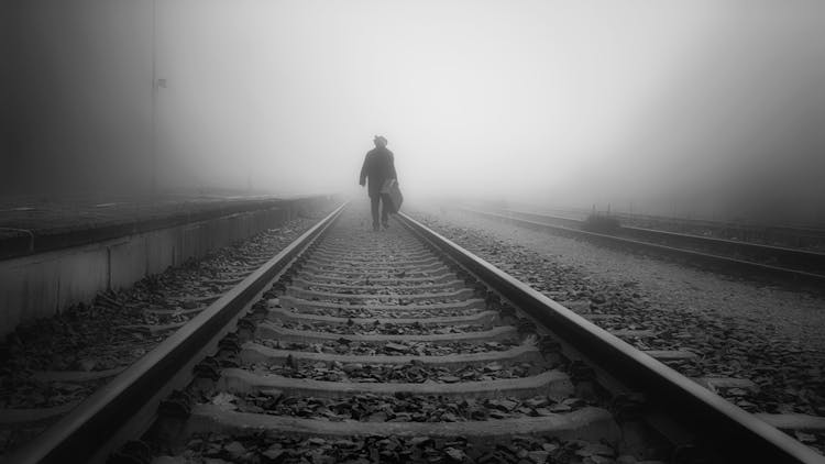 Man Carrying A Luggage Walking On A Railroad Track