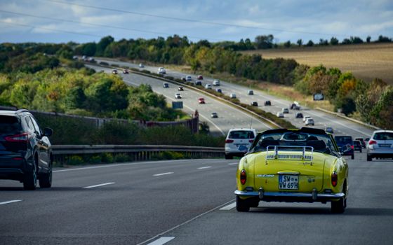 A vintage car travels on a German highway amid lush countryside scenery, highlighting automotive travel.