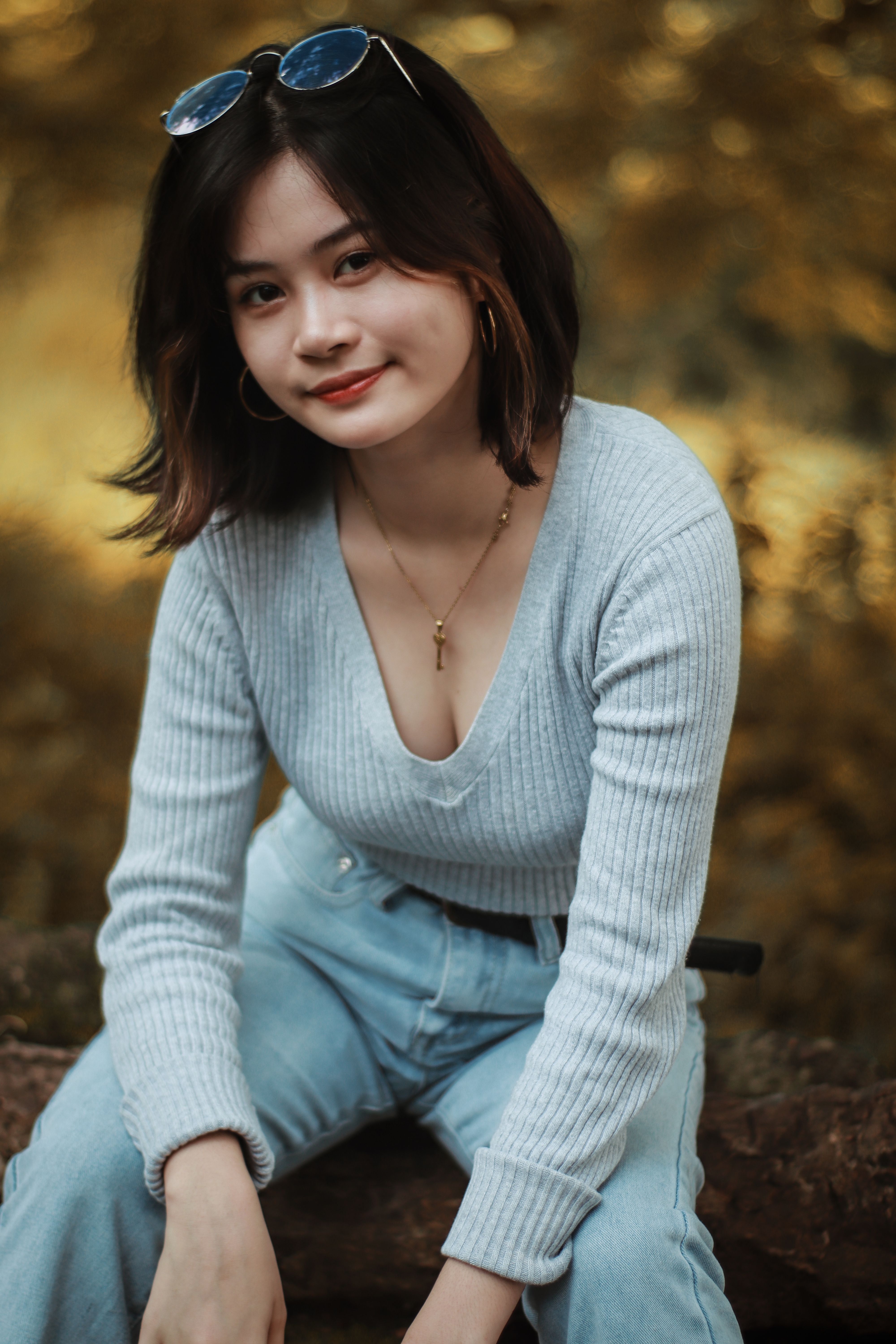 Smiling young Asian woman posing outdoors in casual attire, embracing nature.