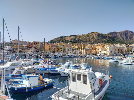 Vibrant boats docked at Porticello harbor in Sicily with hillside town view.