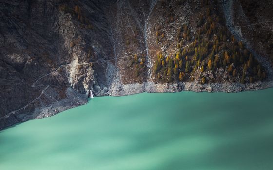 Stunning aerial view of turquoise lake surrounded by rocky mountains and autumn trees in Lombardy, Italy.
