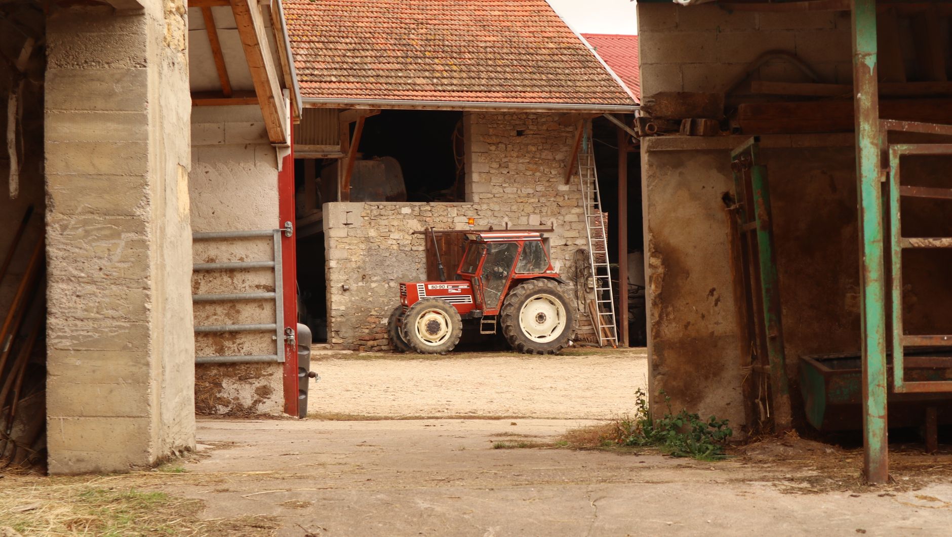 A vintage tractor parked inside a barn in a rustic farm setting.