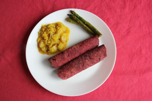 A delicious vegan dish featuring beetroot rolls, asparagus, and lauki curry on a white plate.