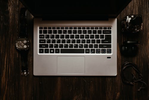 Silver Laptop on the Wooden Surface with a Wristwatch and Earphones