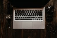 Silver Laptop on the Wooden Surface with a Wristwatch and Earphones