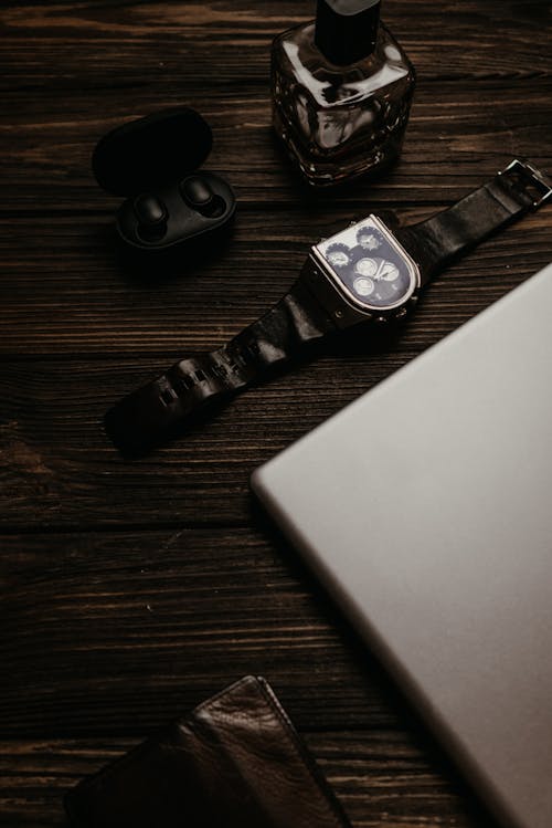 An Analogue Watch with Earphones and Perfume Bottle on a Wooden Surface