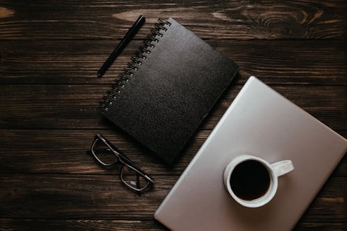 Black Notebook and Pen Near a Laptop on the Wooden Surface