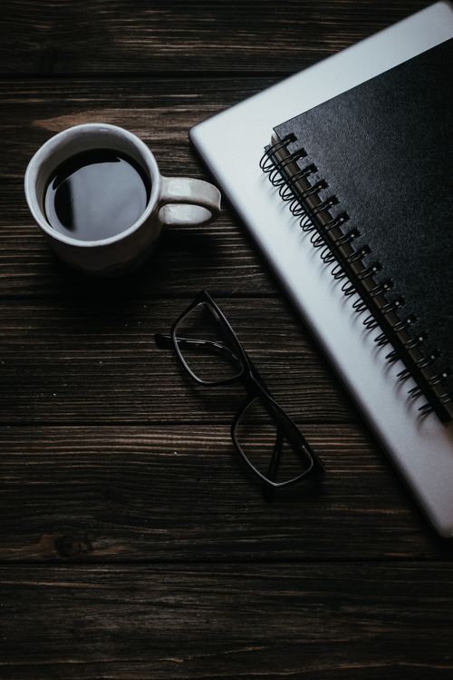 Free Top view of a coffee cup, eyeglasses, notebook, and laptop on wooden surface. Stock Photo