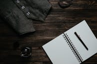 A Black Denin Vest Beside a Perfume Bottle and a Notebook