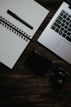 Stylish top view of a desk workspace featuring a laptop, notebook, pen, and wallet on a wooden surface.