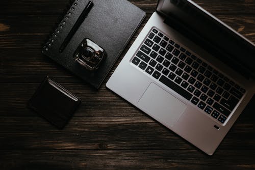 Black Notebook and Wallet Beside a Laptop