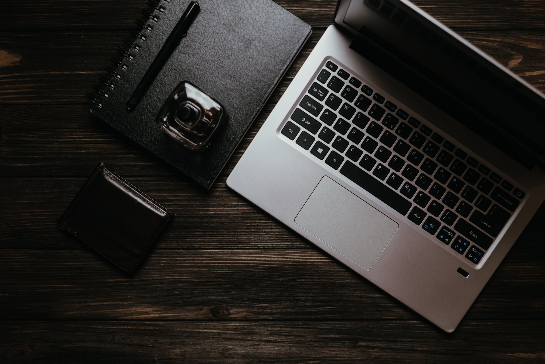 Flat lay of a laptop, notebook, pen, and wallet on a wooden table.