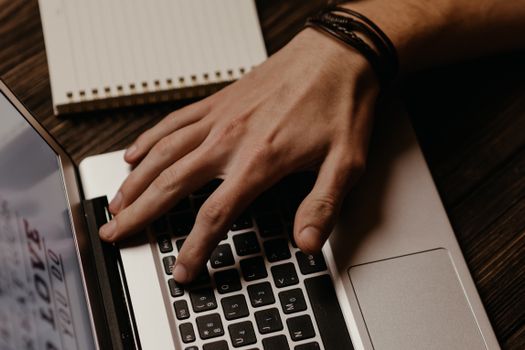 A close-up image showing a hand typing on a laptop with a notebook in the background.