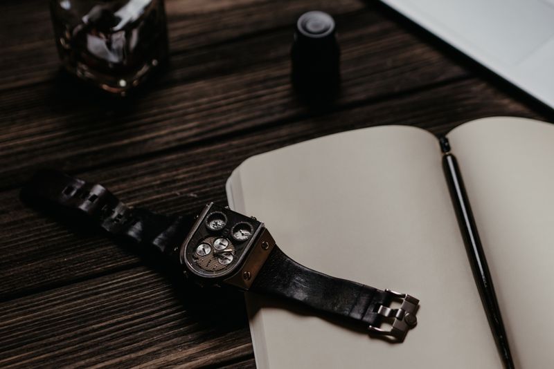 A watch and pen resting on a notebook in low warm light