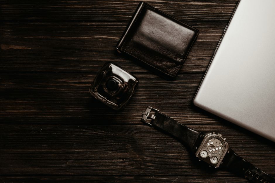 Stylish flat lay showcasing wallet, watch, and laptop on wooden surface.