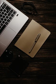 A warm, inviting workspace featuring a laptop, notebook, and pen on a wooden surface.