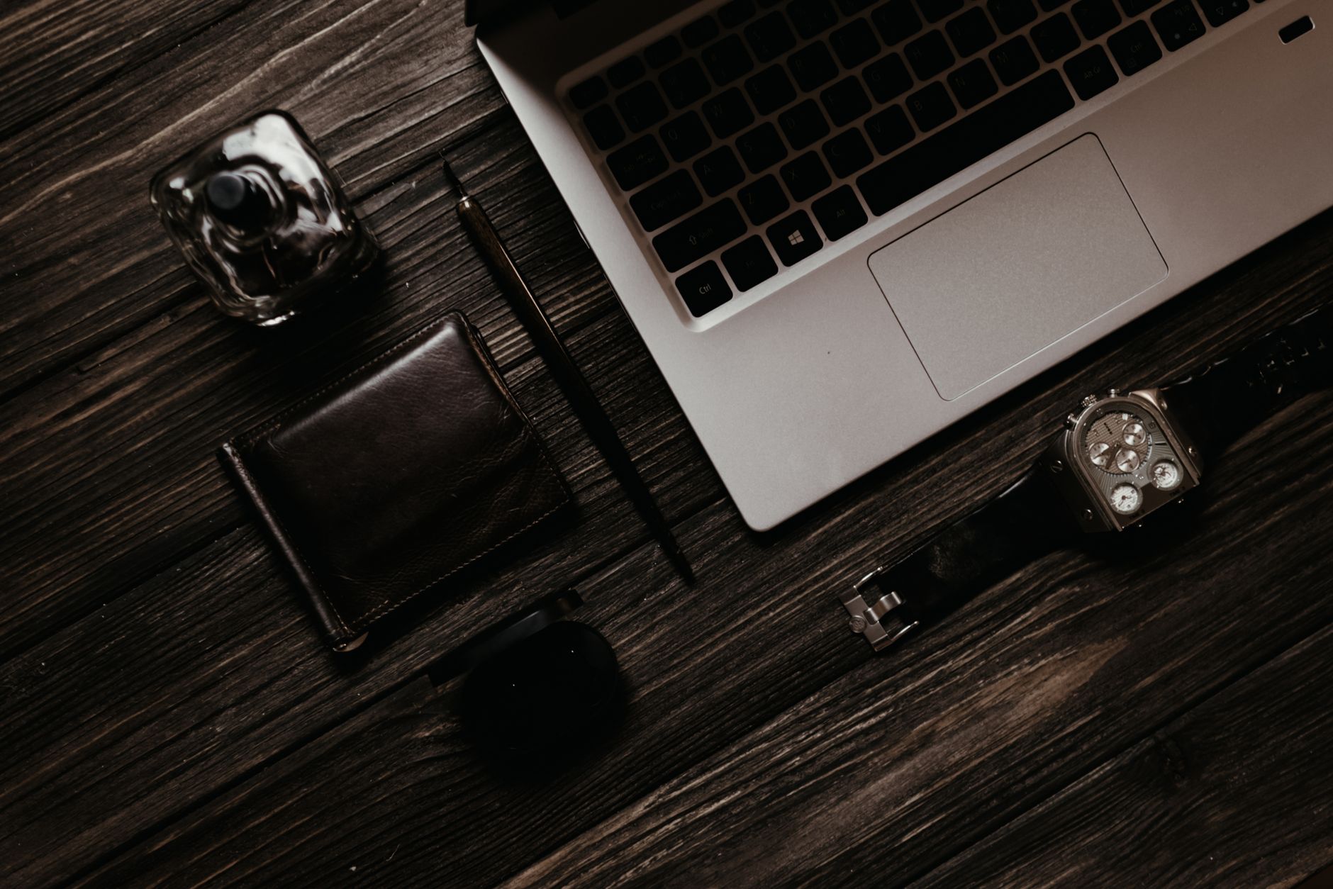 Elegant flat lay of a laptop with accessories like wallet, wristwatch, and perfume on a wooden table.