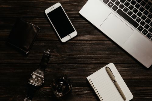 Free Top view of a workspace featuring a laptop, smartphone, notepad, and watch on a wooden table. Stock Photo