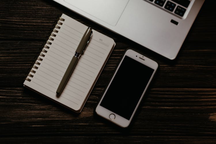 Iphone And Notepad On Wooden Table