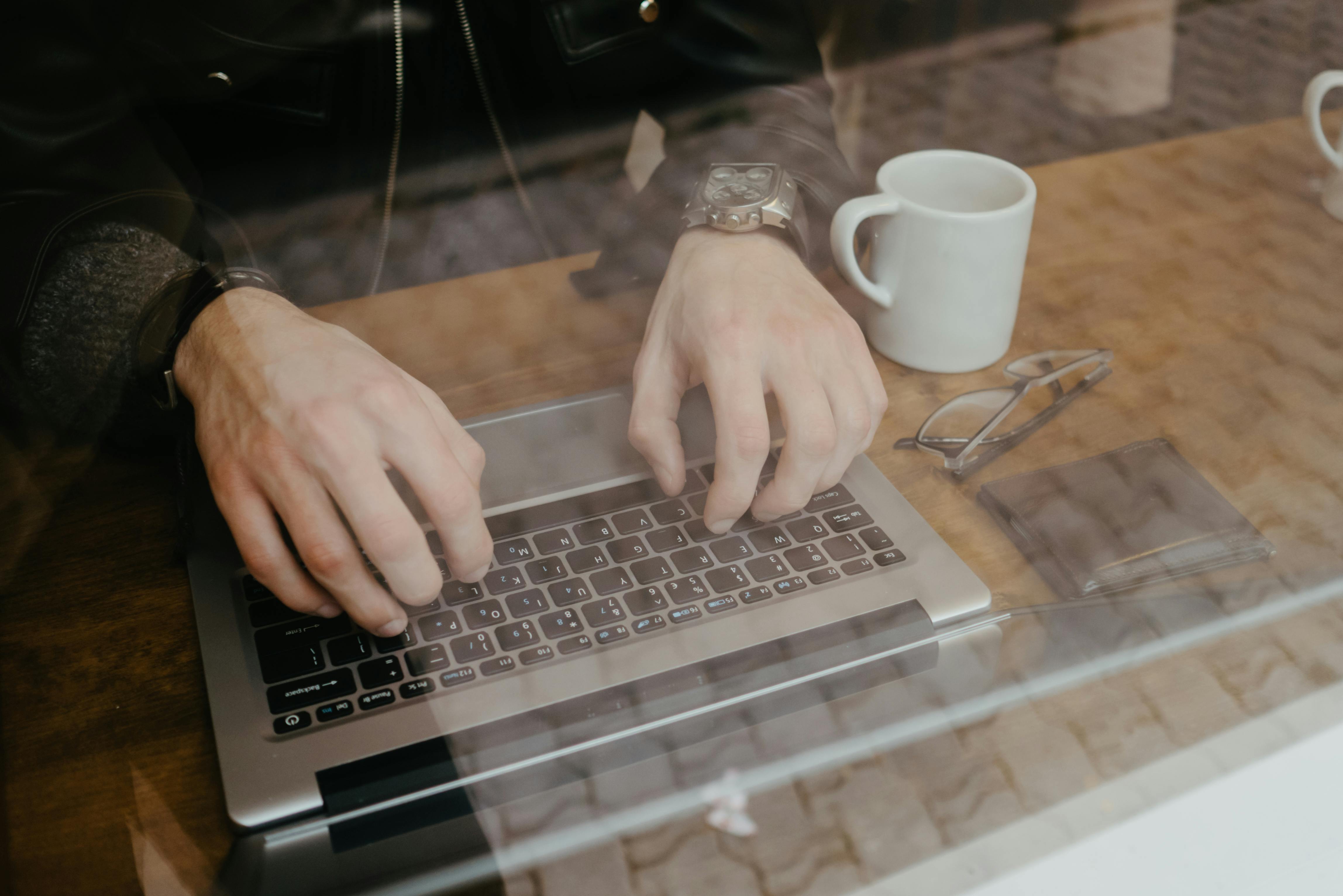 在办公环境中，手在笔记本电脑上打字，旁边放着一个陶瓷杯