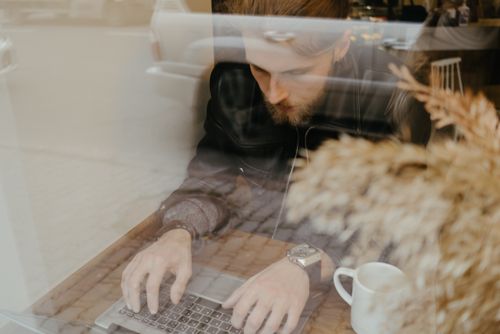 Free A man in a café working on a laptop with a coffee mug on the table. Stock Photo
