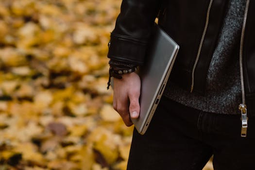 Close-up of a person carrying a laptop during fall, surrounded by autumn leaves.