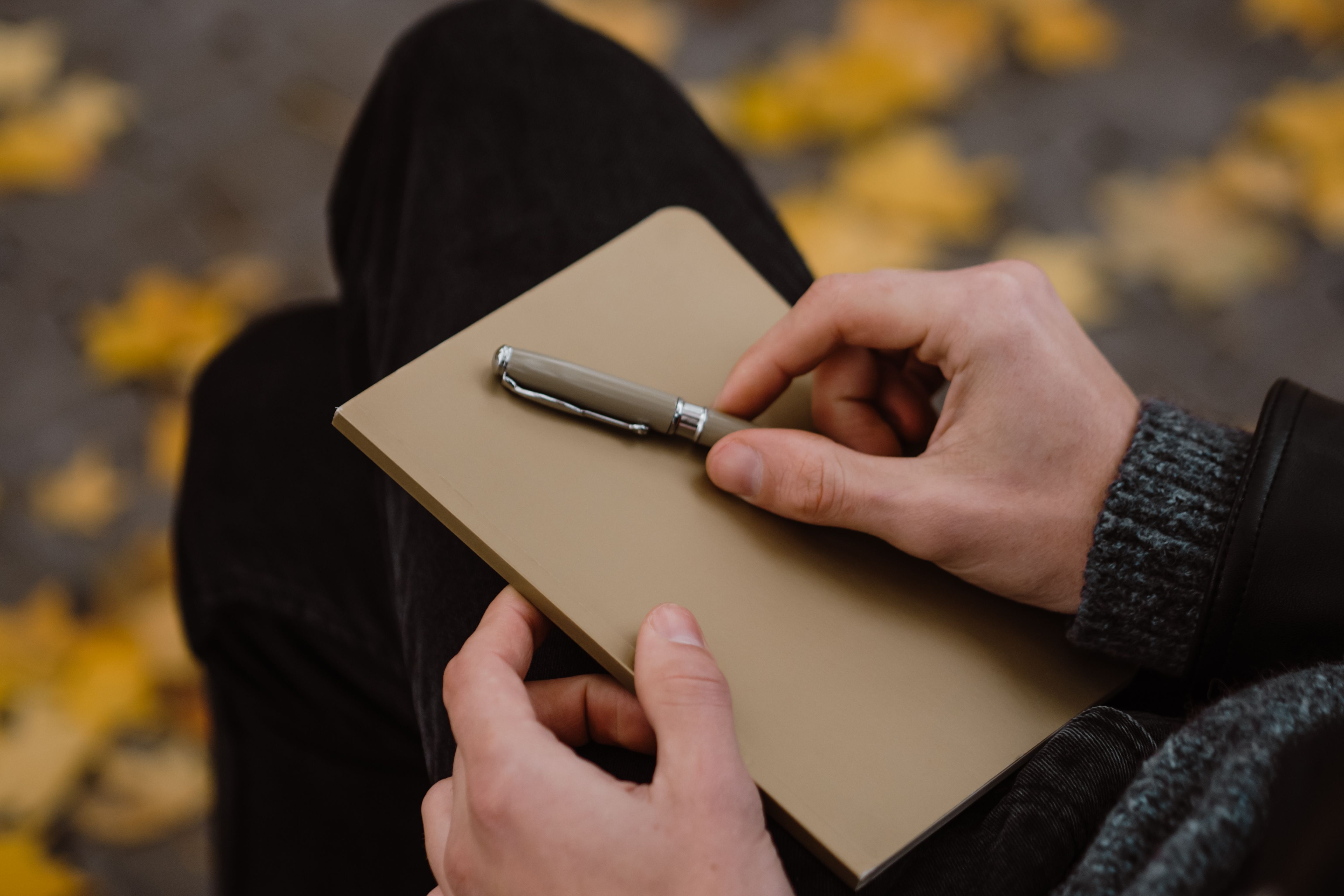 Hands holding a notebook and pen in a cozy autumnal setting. Perfect for journaling themes.