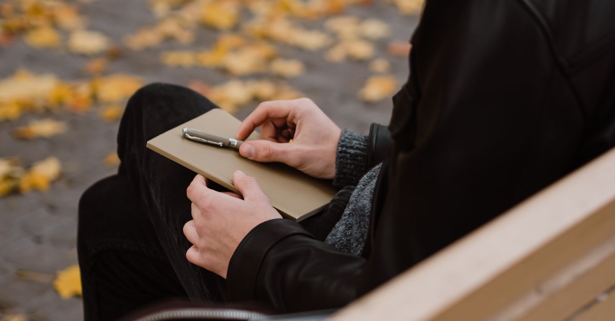 A person sitting in a quiet church pew, looking at a notebook with a pen in hand, deep in thought