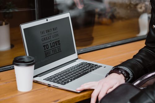 Free A person using a laptop with motivational quote, alongside coffee cup in a modern cafe setting. Stock Photo