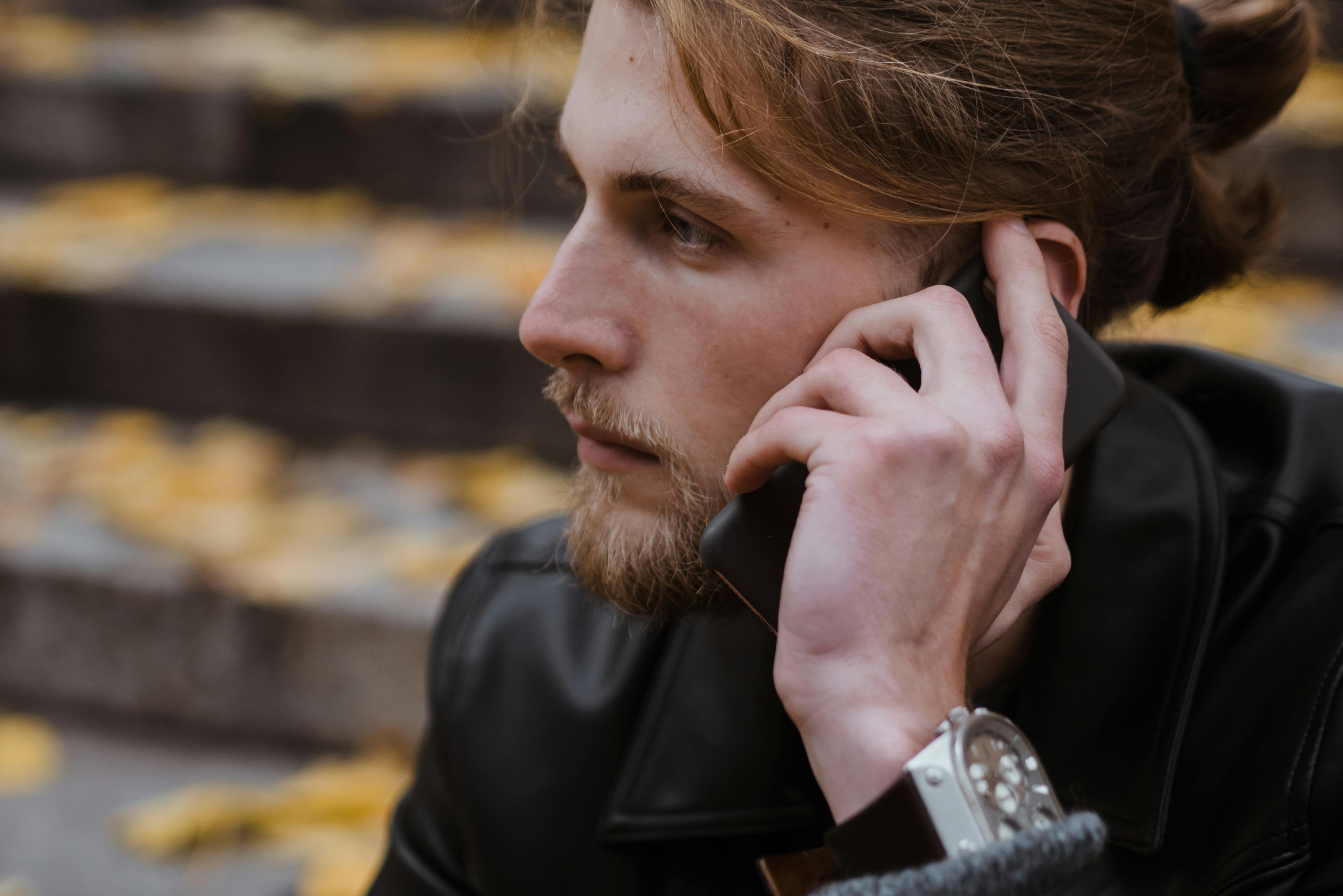Close-up of a young man with a beard talking on his phone outdoors in autumn.